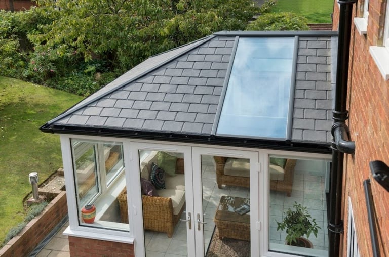 Aerial view of a modern conservatory with glass doors, white frames, and a slate roof with skylight overlooking a green garden