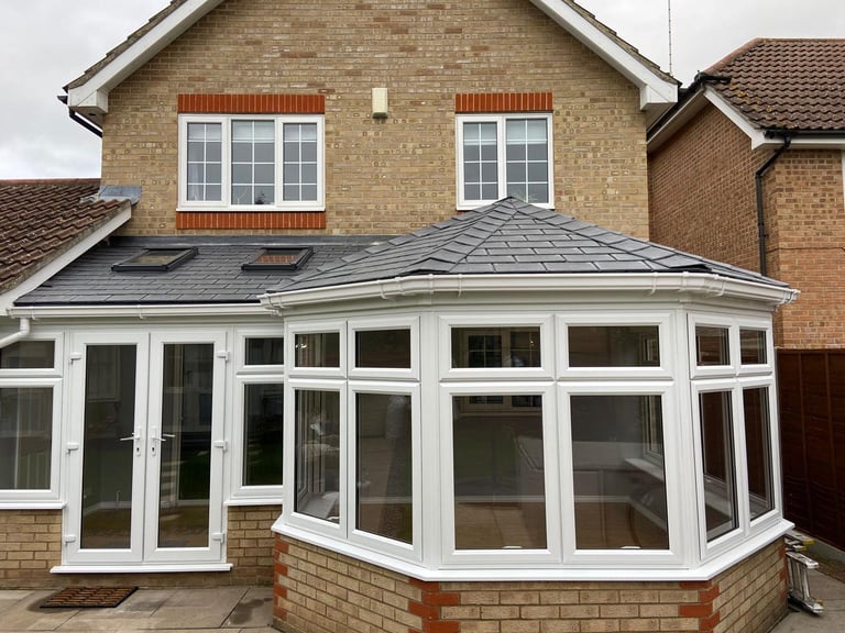 Brick house with white uPVC conservatory extension featuring a gray tiled roof and multiple glass panels