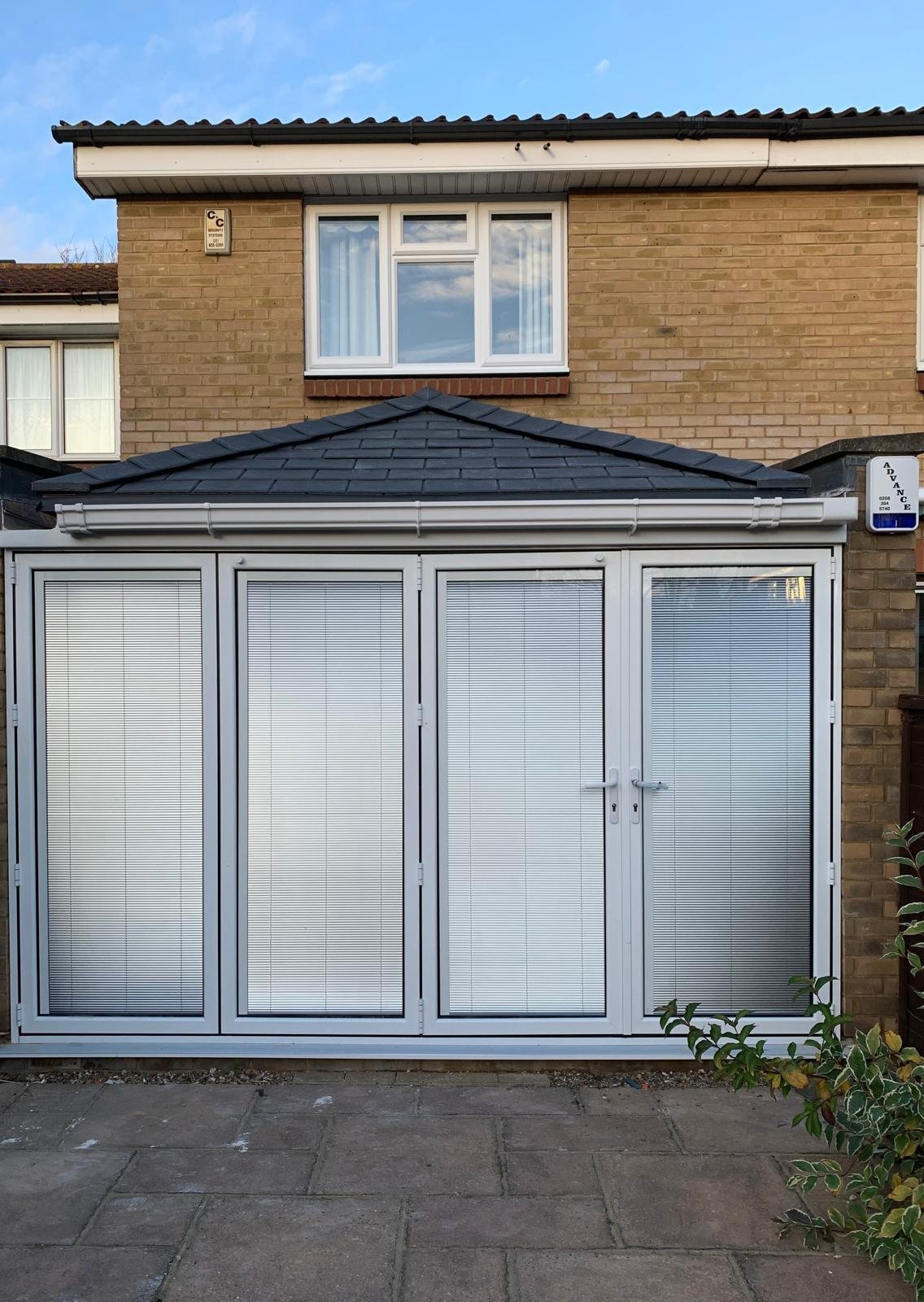 Modern aluminum bifold doors with grid pattern attached to brick house with dark roof and upper window