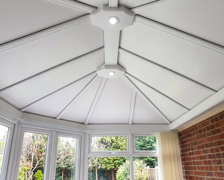 Interior view of a white coffered conservatory ceiling with skylights and large windows overlooking a garden