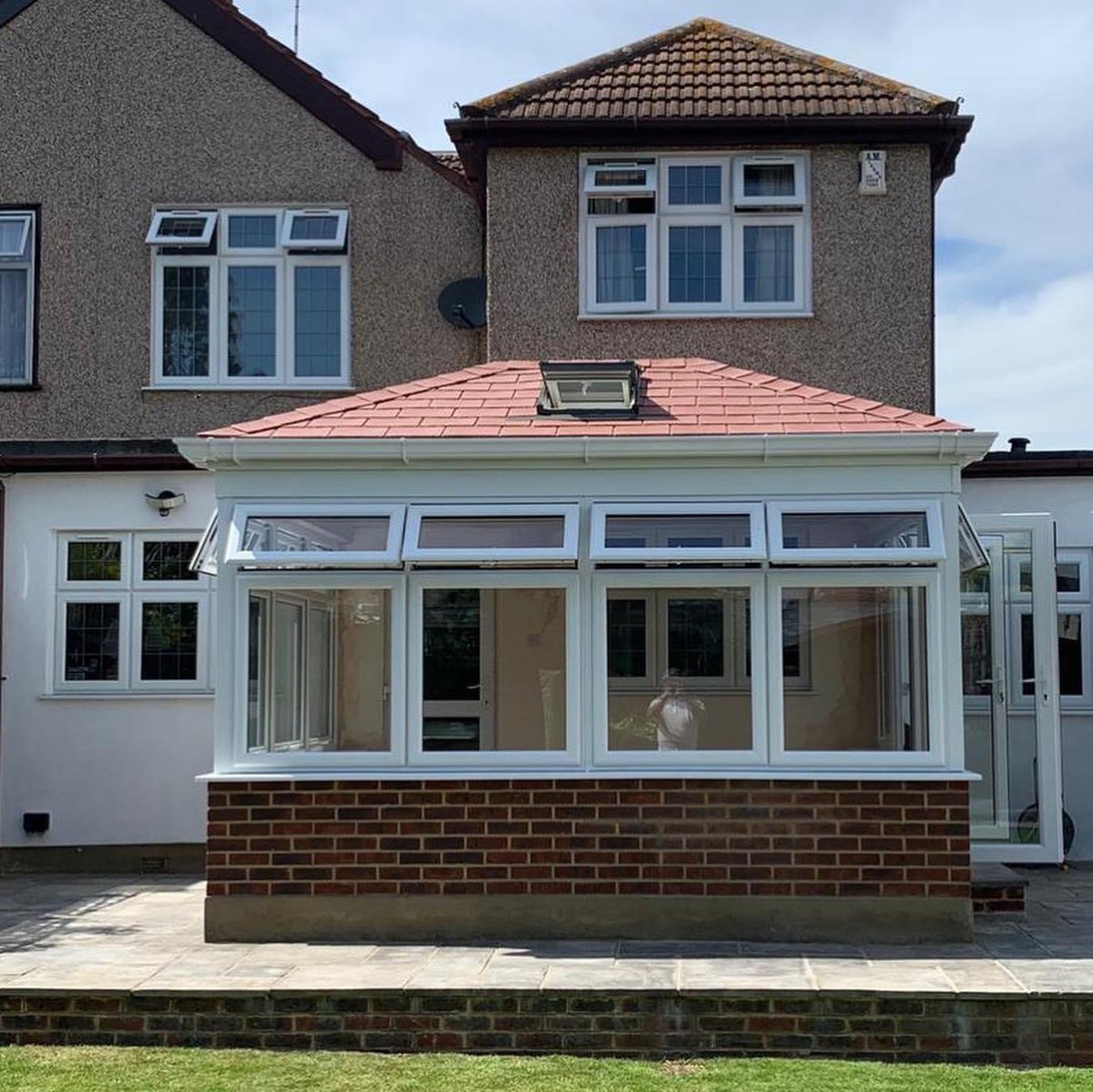 Modern white conservatory with red tiled roof extension attached to brick suburban home