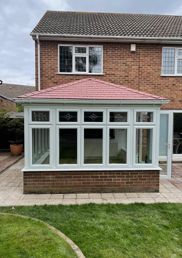 Modern brick house with white-framed glass conservatory featuring a pink pyramid roof and brick base, surrounded by patio and lawn