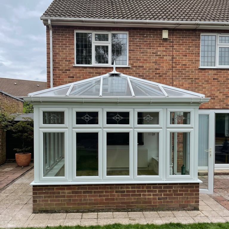 Before: White conservatory with glass roof and paneled windows attached to brick house with paved patio