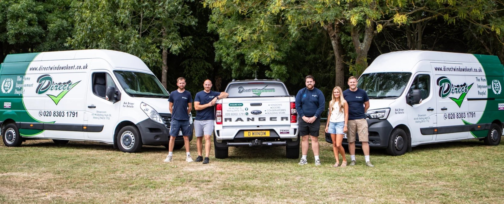 Team members stand between two green and white service vans and a utility vehicle on grass with trees in background